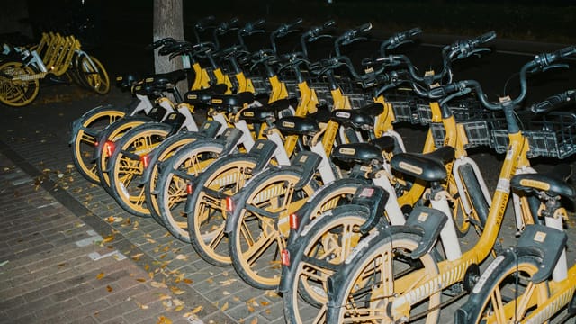 Nighttime view of neatly parked yellow rental bicycles lined up on a city street sidewalk.