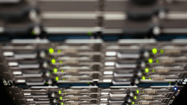 Close-up of a network server rack with blinking LEDs, showcasing Ethernet connections and patch panels.