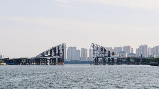 Open drawbridge over a river with a city skyline in the background under a clear sky.