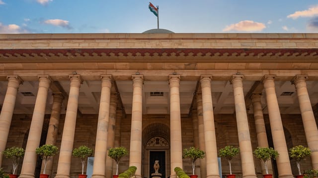 Government building in New Delhi featuring columns and an Indian flag under a vibrant sky.