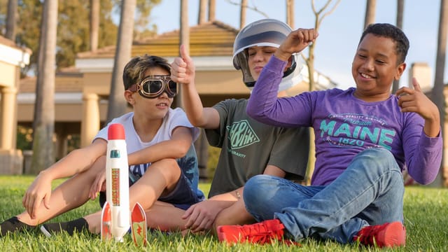 Three boys enjoying playtime with a toy rocket on a sunny day.