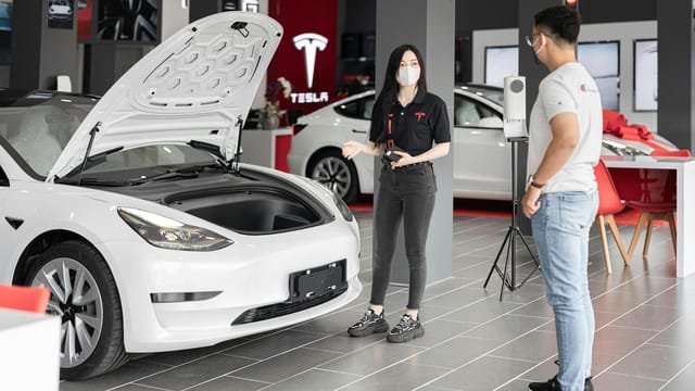 A customer talks with a sales representative about a Tesla Model 3 in a car dealership, showcasing the electric car's features.
