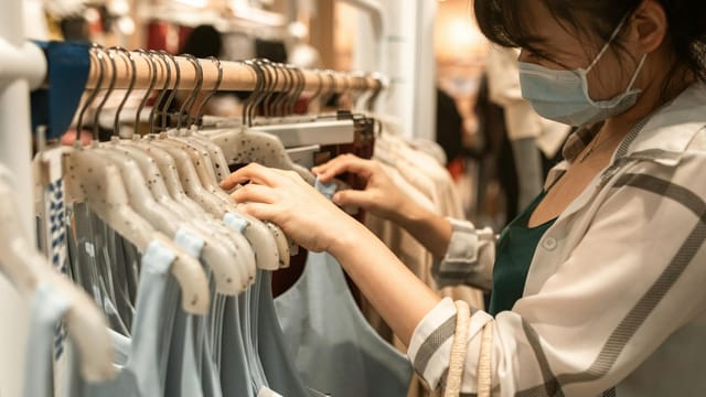 Woman wearing a face mask shopping for apparel indoors, emphasizing safety and fashion.