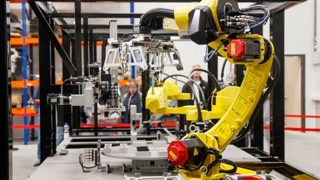 Illustrative image: Close-up of a yellow industrial robotic arm in action at a modern manufacturing facility.
