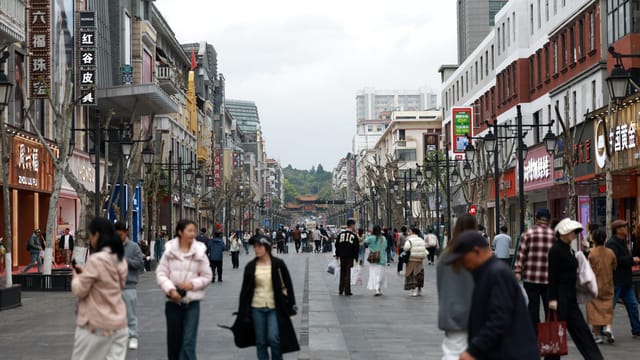 Crowded shopping street with people walking past shops and cafes in an Asian city center.