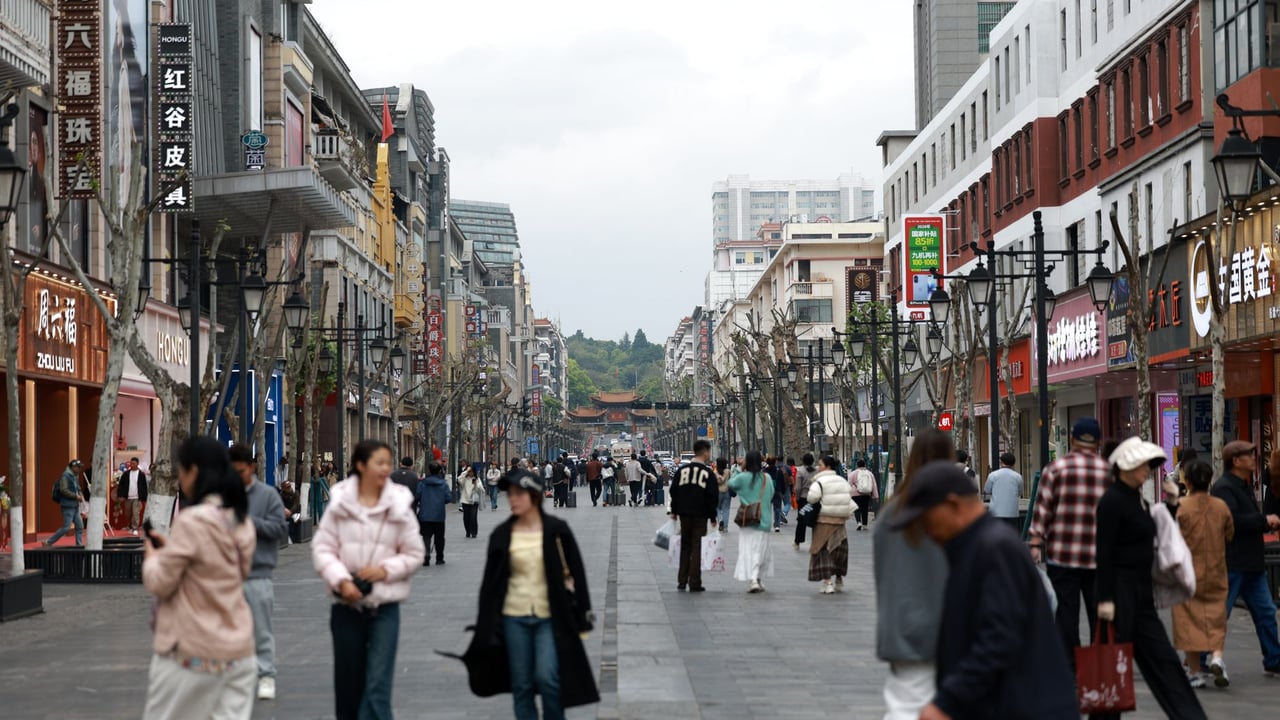 Crowded shopping street with people walking past shops and cafes in an Asian city center.