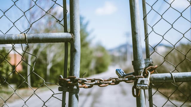 Close-up of a locked chain link fence with rusty chains and padlock, outdoors, in bright daylight.