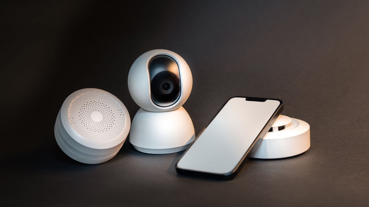 A sleek smartphone with modern smart home devices on a minimalist gray background.