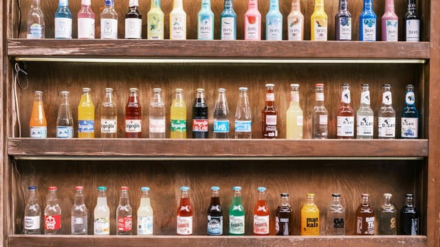 A vibrant collection of vintage soda bottles displayed on wooden shelves, showcasing diverse colors and labels.