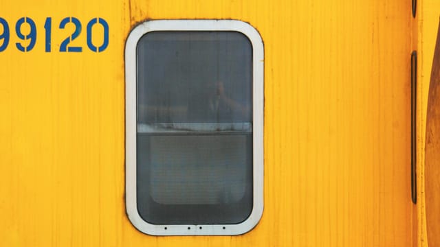 Close-up of a yellow train car featuring a window and number 99120 in bold blue.