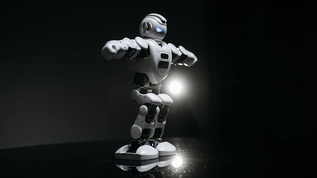 White humanoid robot with glowing eyes standing on a reflective black surface in studio lighting.