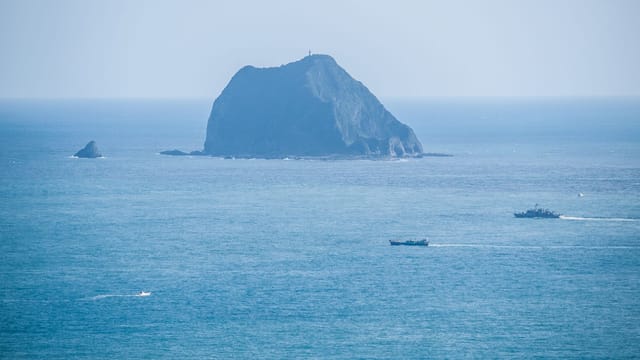 Island surrounded by vast ocean, boats sailing under clear skies. Perfect for travel themes.