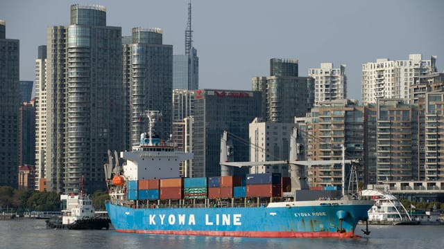 A blue container ship in front of a modern urban skyline, reflecting global trade.