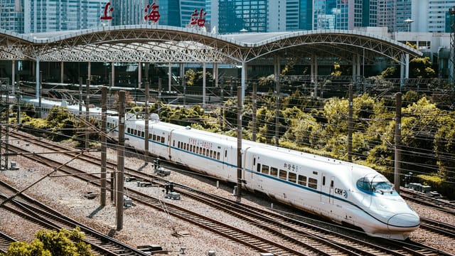 A high-speed train passing through Shanghai Railway Station with city skyline in the background.