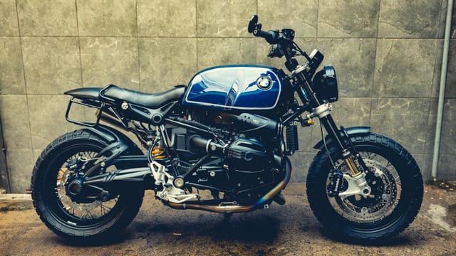 Side view of a classic BMW motorcycle with blue tank in an industrial setting.