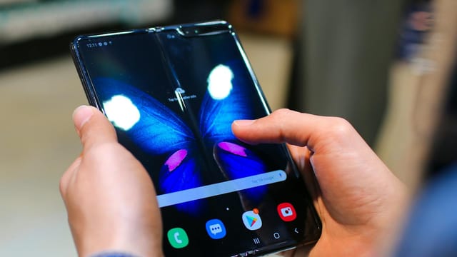 Close-up of hands holding a foldable smartphone showing a butterfly on the screen.