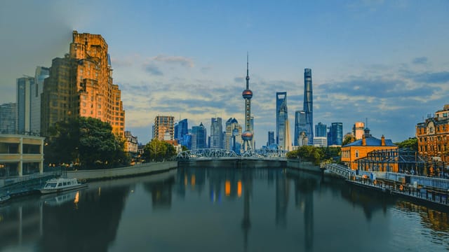 Scenic view of the Shanghai skyline at sunset with the iconic Oriental Pearl Tower reflected in the Huangpu River.