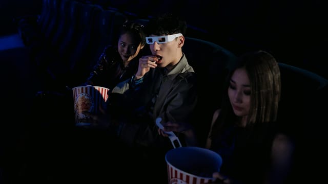 A group of young adults enjoying a movie at the cinema, complete with popcorn and 3D glasses.