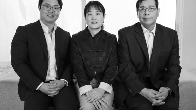Black and white portrait of three professionals in suits sitting indoors.