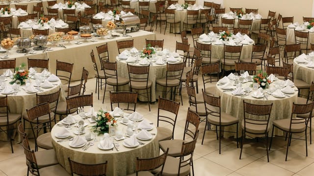 Spacious banquet hall setup with neatly arranged round tables and floral centerpieces, ready for a large event.