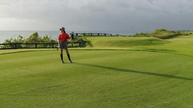 A woman golfer stands on a lush golf course overlooking the sea, capturing the essence of outdoor recreation and relaxation.