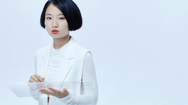 A sleek minimalist portrait of a serious woman holding a transparent glass panel.