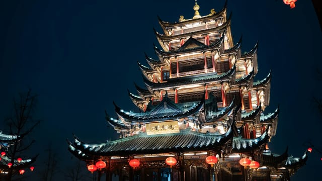 Illuminated traditional Chinese temple in Chongqing, adorned with red lanterns during night time.