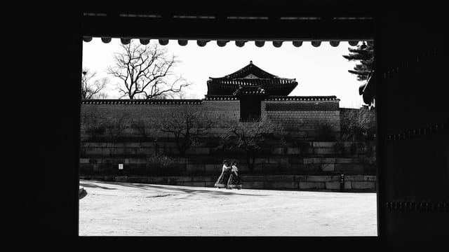A black and white view of a traditional palace in Seoul, framed by a wooden gate, capturing a serene winter scene.
