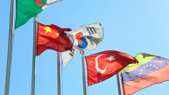 Five national flags from different countries waving on flagpoles under a clear blue sky