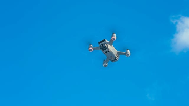 From below of quadcopter with small propellers and motors flying in vibrant blue sky
