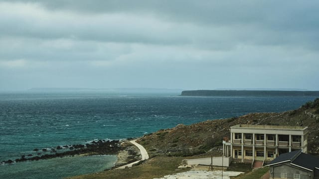 Aerial view of a deserted building by the coast in Wangan, Taiwan, under a cloudy sky.