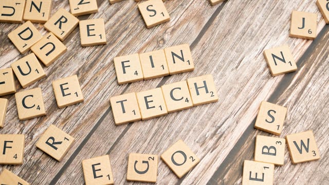 Fintech spelled out with wooden letter tiles on a rustic wooden background.