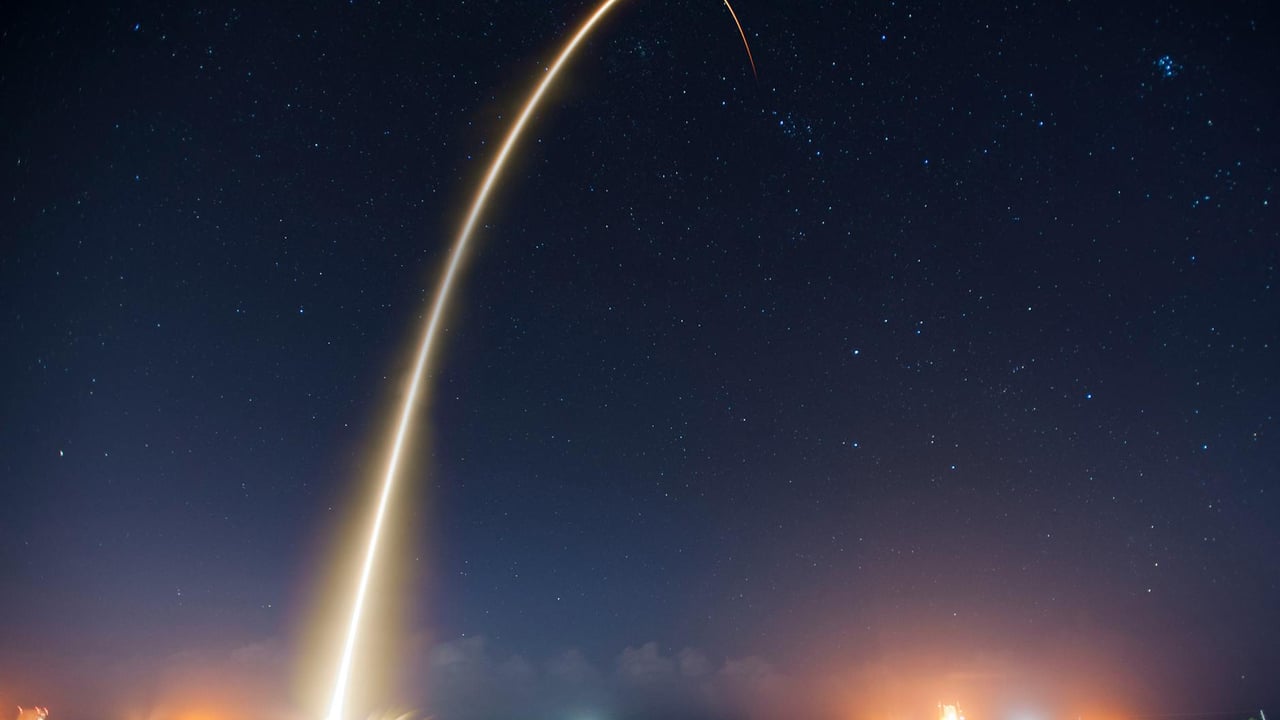Spectacular long exposure of a rocket launch under a clear, starry night sky showcasing the trail.