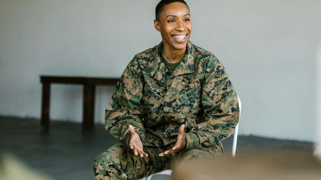 A happy female soldier in uniform smiling and talking indoors.