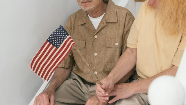 Senior couple sitting on steps indoors, holding a small United States flag together.