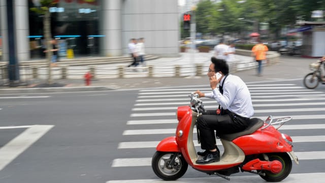 Businessman riding a red scooter while talking on the phone in Shanghai, China.