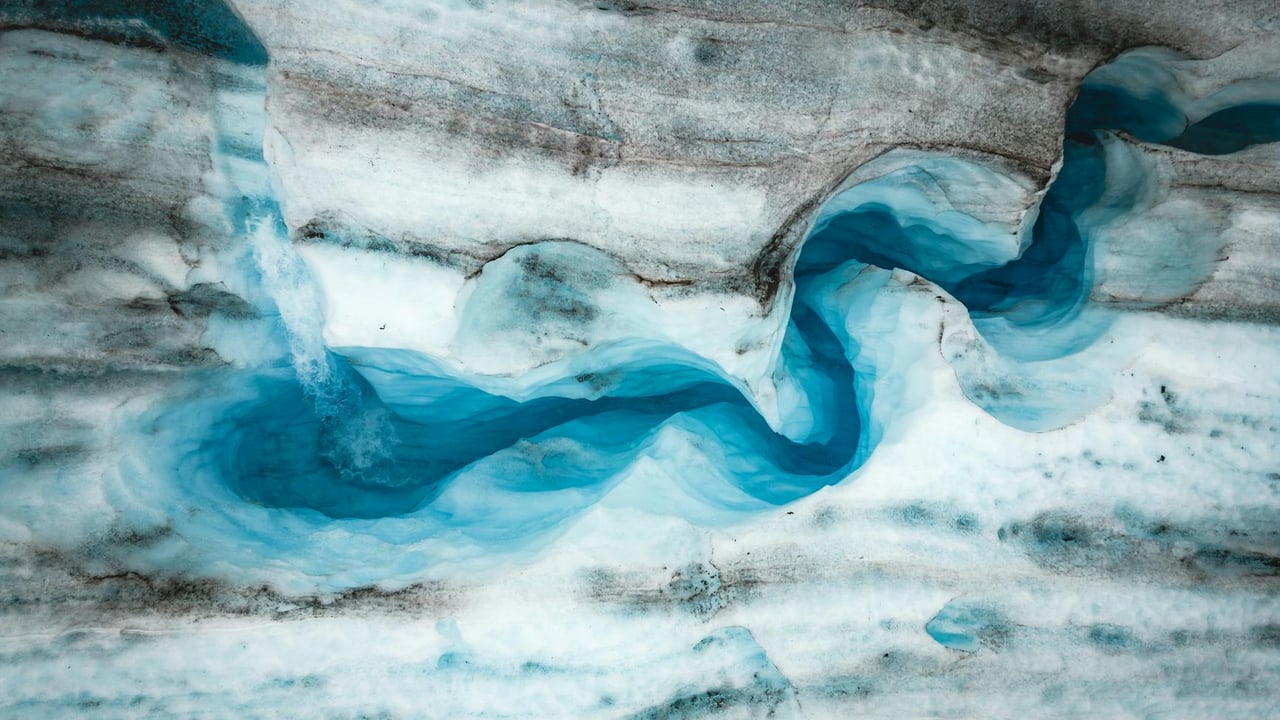 Stunning aerial view of a winding glacier with vibrant blue ice, capturing nature's artistry.
