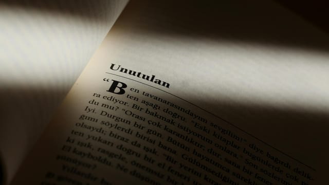 Moody close-up photo of a book page partially lit, highlighting text in Turkish.