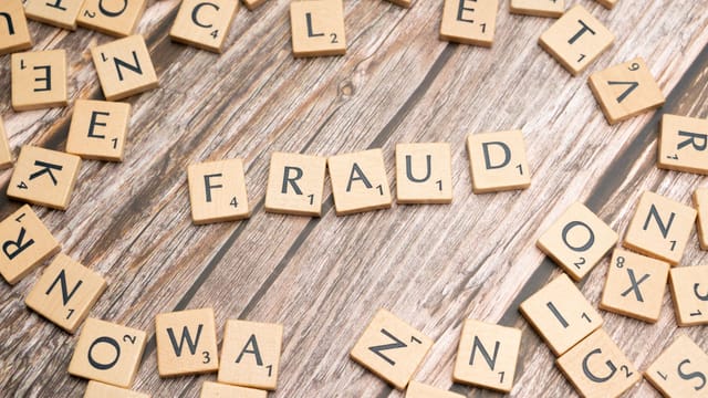 Alphabet tiles arranged to spell 'fraud' on a wooden surface, symbolizing deception.