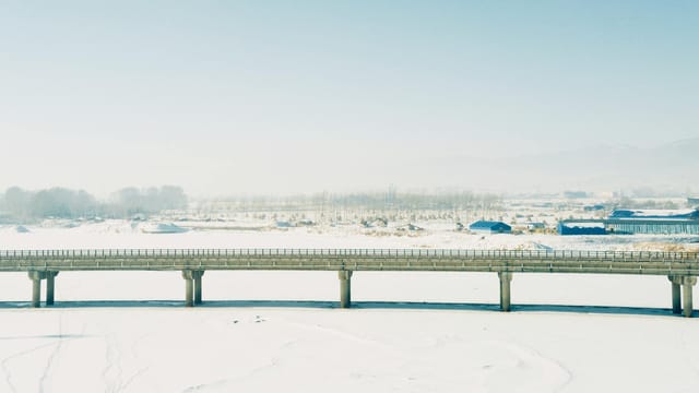 Aerial view of a snowy bridge over a frozen river in Jilin, China on a sunny winter day.