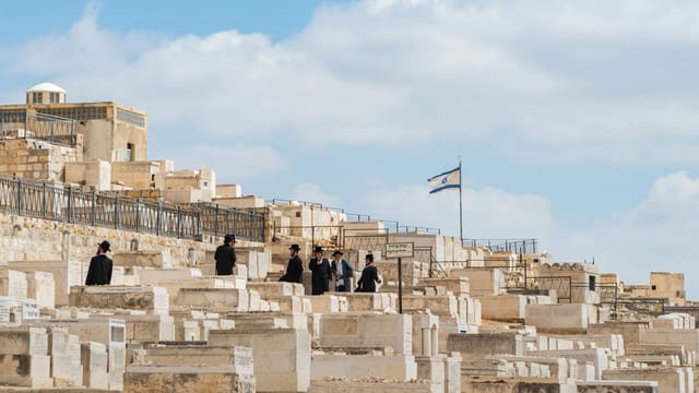Orthodox Jewish men gather at Mount of Olives Cemetery in Jerusalem, Israel, under a clear sky.