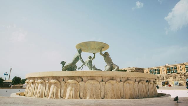 The iconic Triton Fountain in Malta under a clear blue sky, showcasing its marble sculptures.