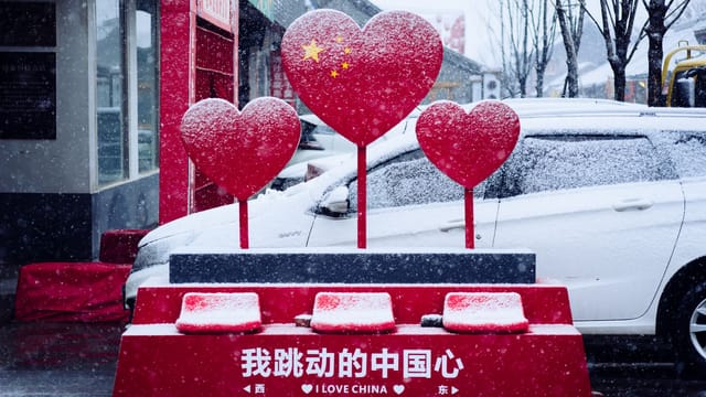 Snow-covered heart sculptures form a vibrant street installation with 'I Love China' text.