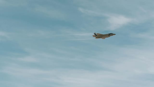 A military fighter jet soaring through a clear blue sky with contrails visible.