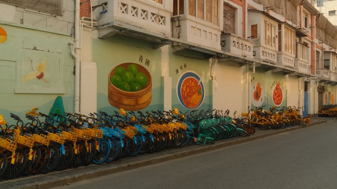 Colorful shared bicycles parked along a mural-lined street in Shanghai, China, showcasing vibrant urban culture.
