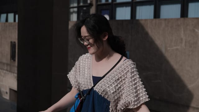 Stylish woman in knitwear posing outdoors in urban setting, wearing glasses.