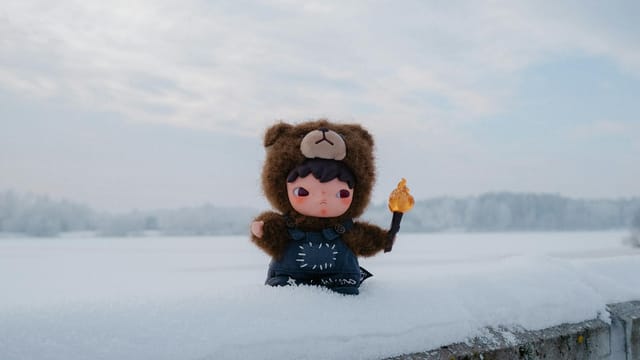 Adorable toy in bear costume holding object, set against a snowy winter backdrop.