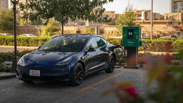 Tesla Model 3 charging at an urban electric vehicle station during daytime.