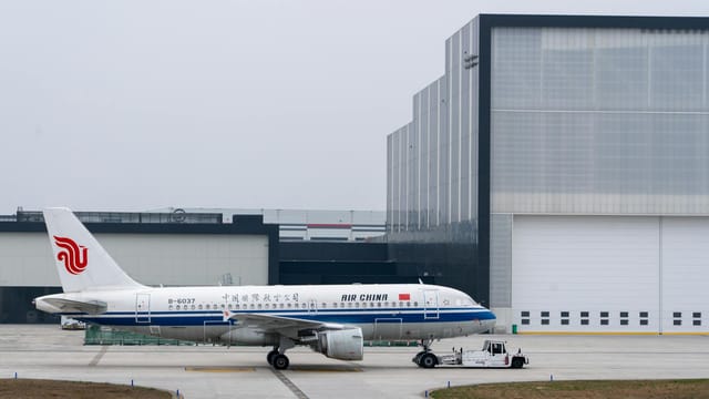 Air China plane parked at an airport hangar on a cloudy day, ready for takeoff.