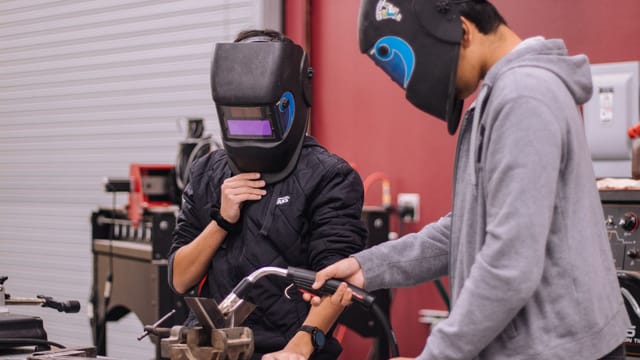 Two welders in protective gear concentrate on a project in a workshop setting.